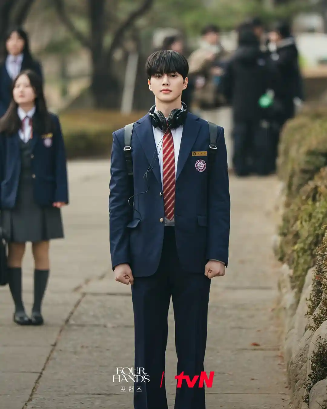 포핸즈 강비오가 교복을 입고 헤드폰을 목에 건 채 서 있는 장면
